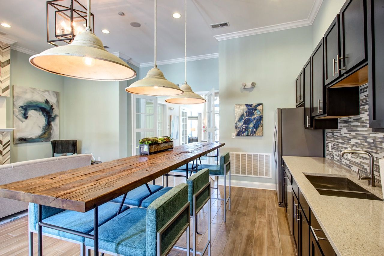 Bright kitchen with a long rustic wood island, blue bar stools, and dark cabinets.