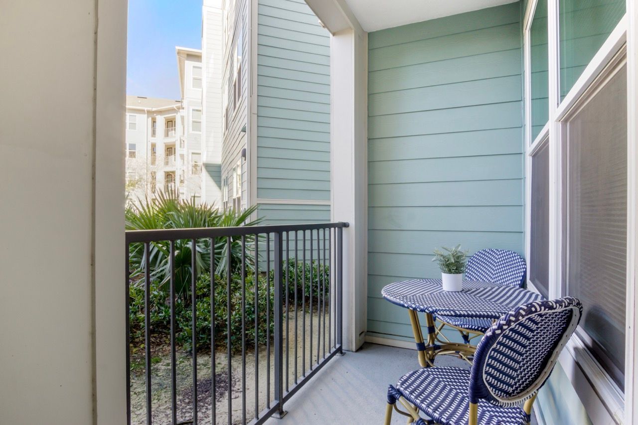 Balcony with blue-green siding, metal railing, and a small round table with two chairs.