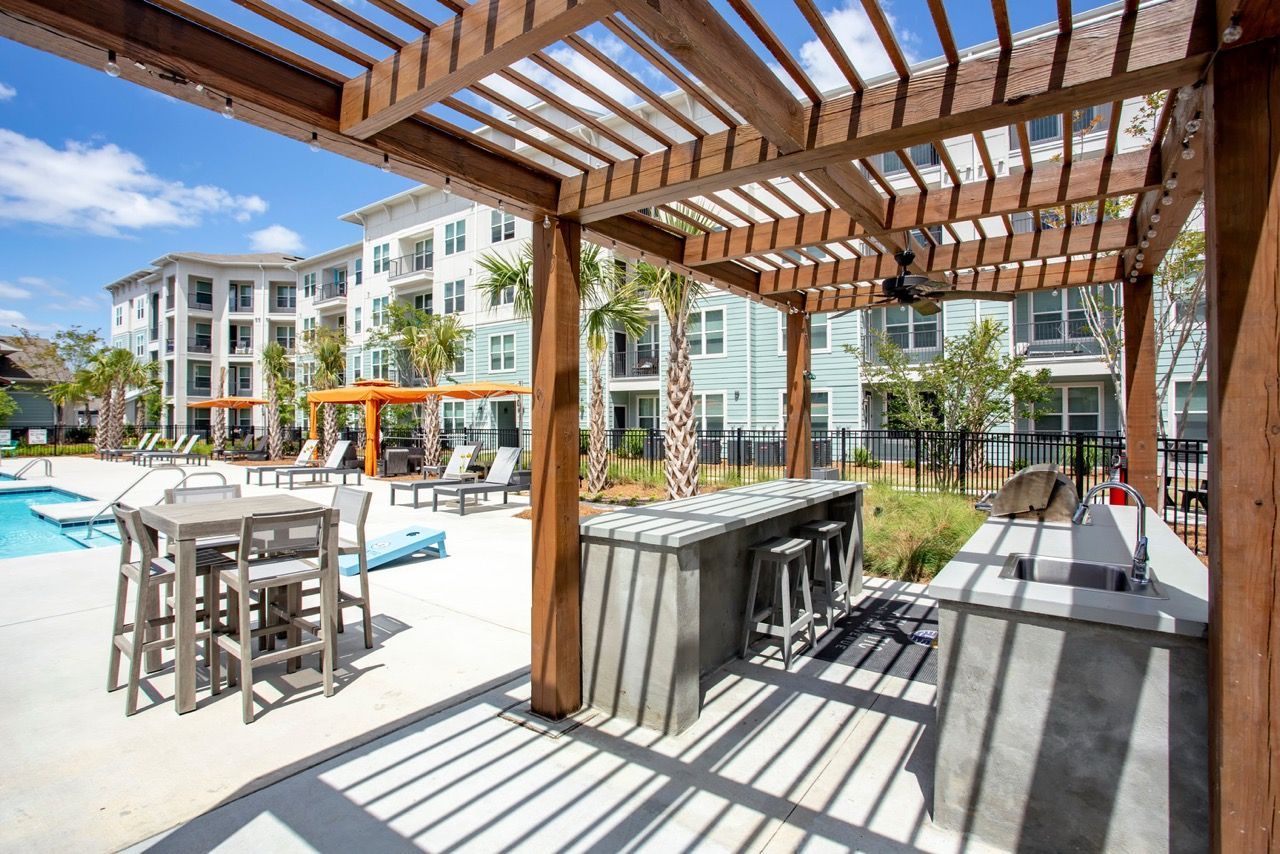 Outdoor pool area with lounge chairs, tables, and a wooden pergola.