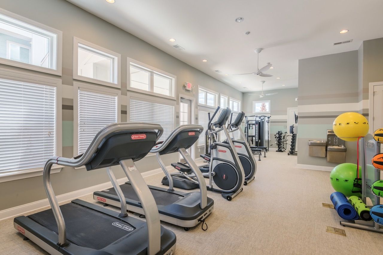 Bright apartment community gym with treadmills, ellipticals, weights, and bright windows.