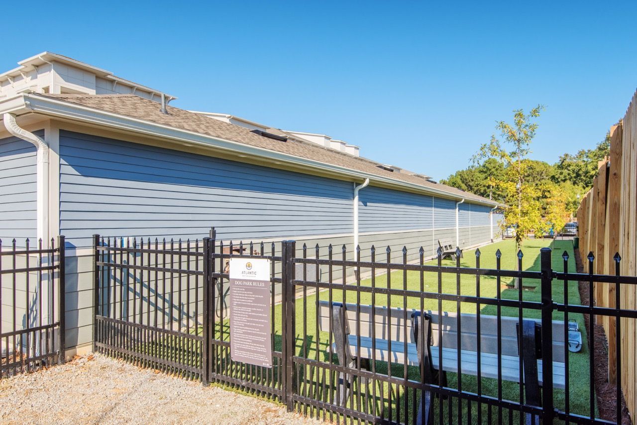 Fenced dog park area beside a blue apartment building, with a bench and sign.