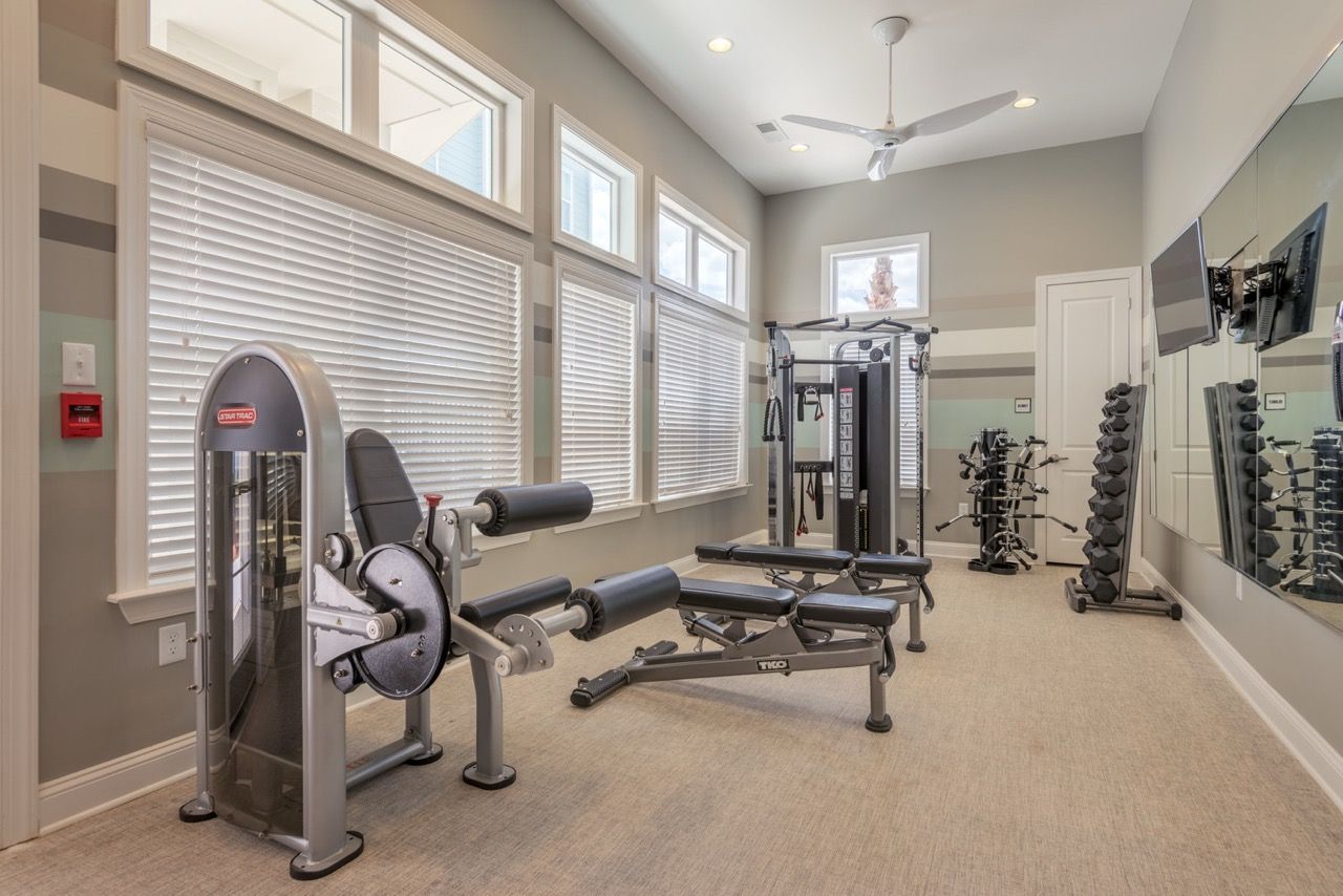 Well-lit community gym with cardio and weight machines, large windows, and mirrors.