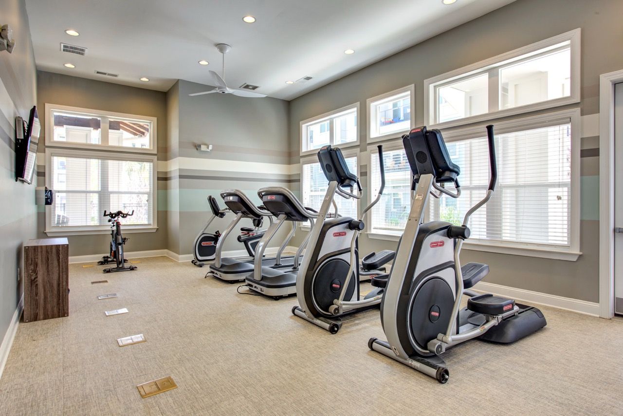 Indoor community gym with multiple cardio machines and large windows.