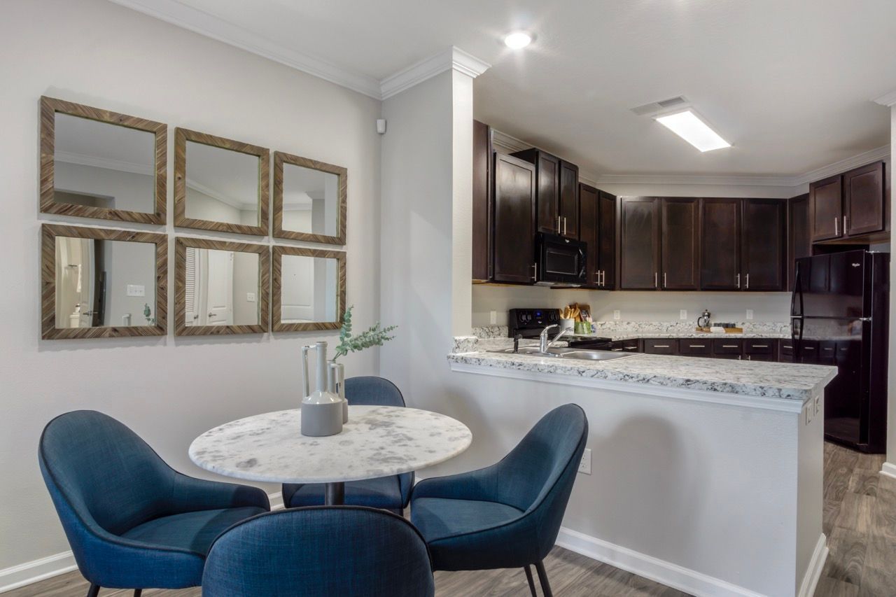 Open dining area with a round marble table and blue chairs next to a granite-counter kitchen.