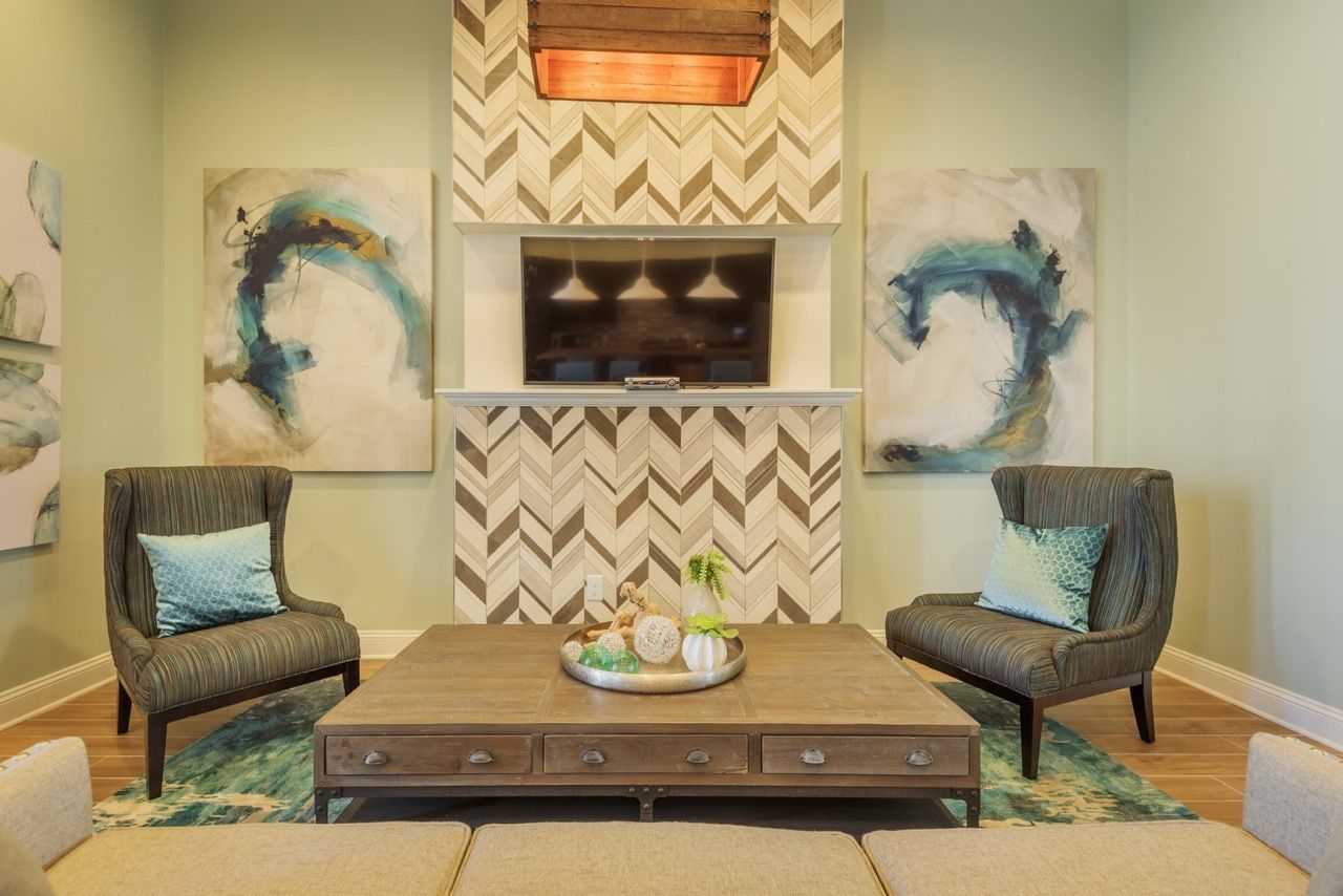 Common area lounge with two striped chairs, a coffee table, abstract art, and TV above a chevron fireplace.