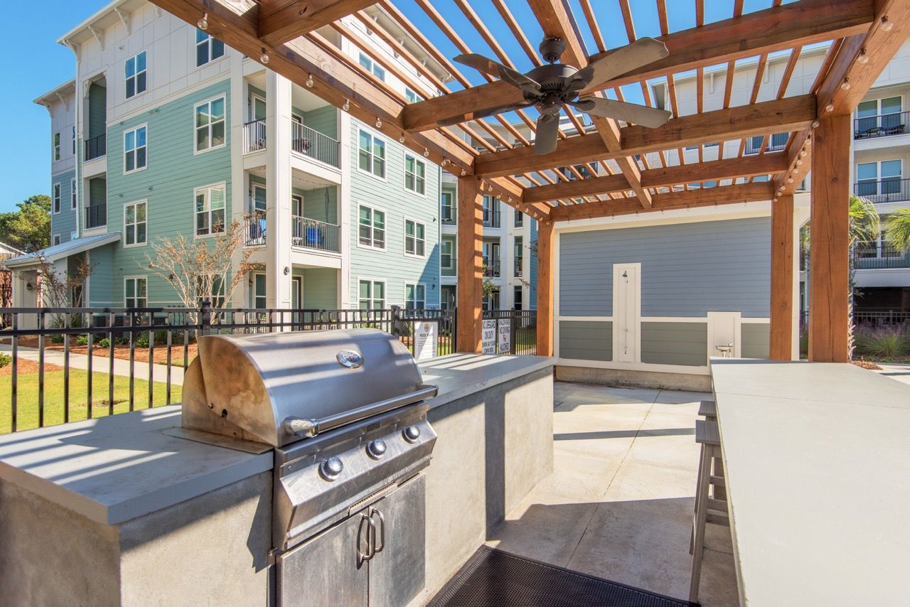 Outdoor community grilling area under a wooden pergola with a built-in grill.
