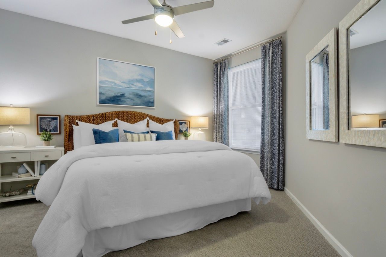 Bedroom in an apartment with a large bed, two nightstands, and windows with curtains.