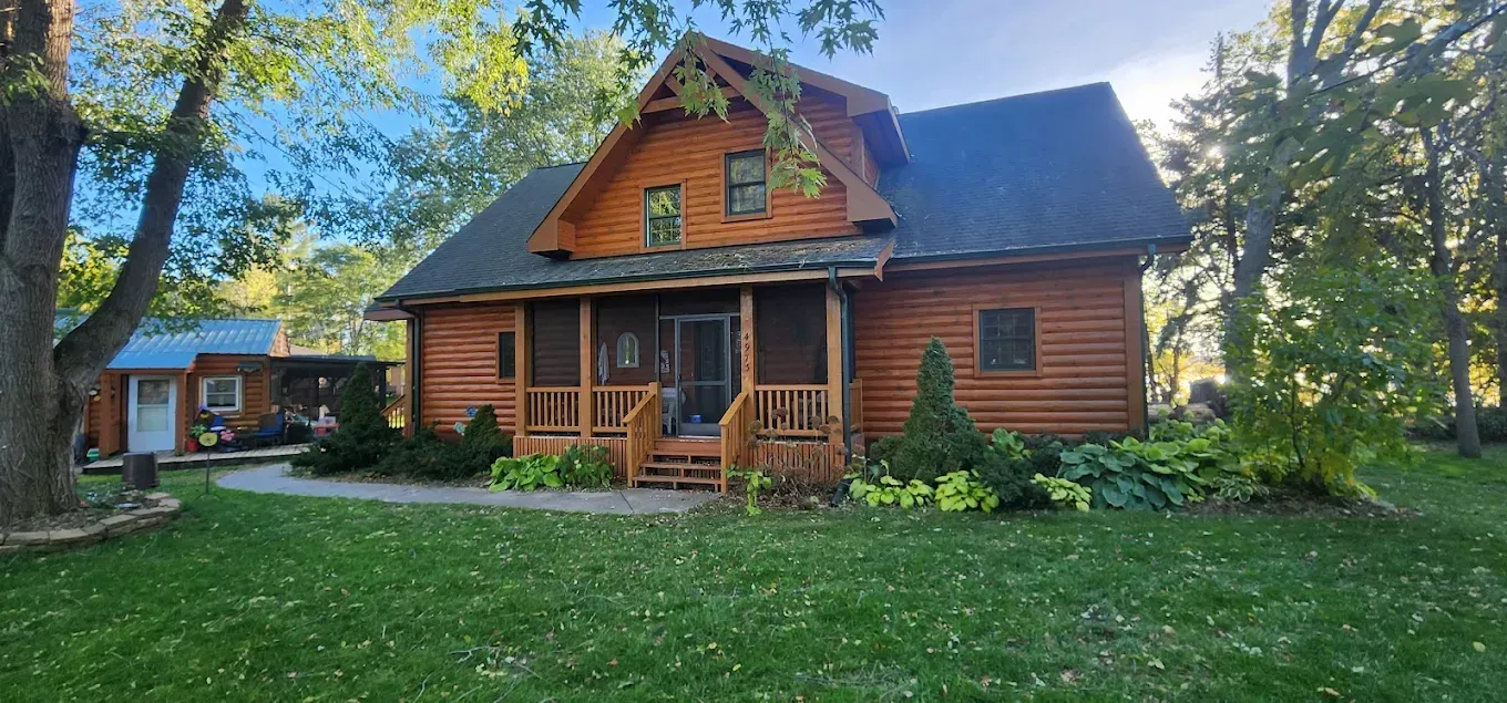 A large log cabin with a screened in porch in the middle of a lush green field.