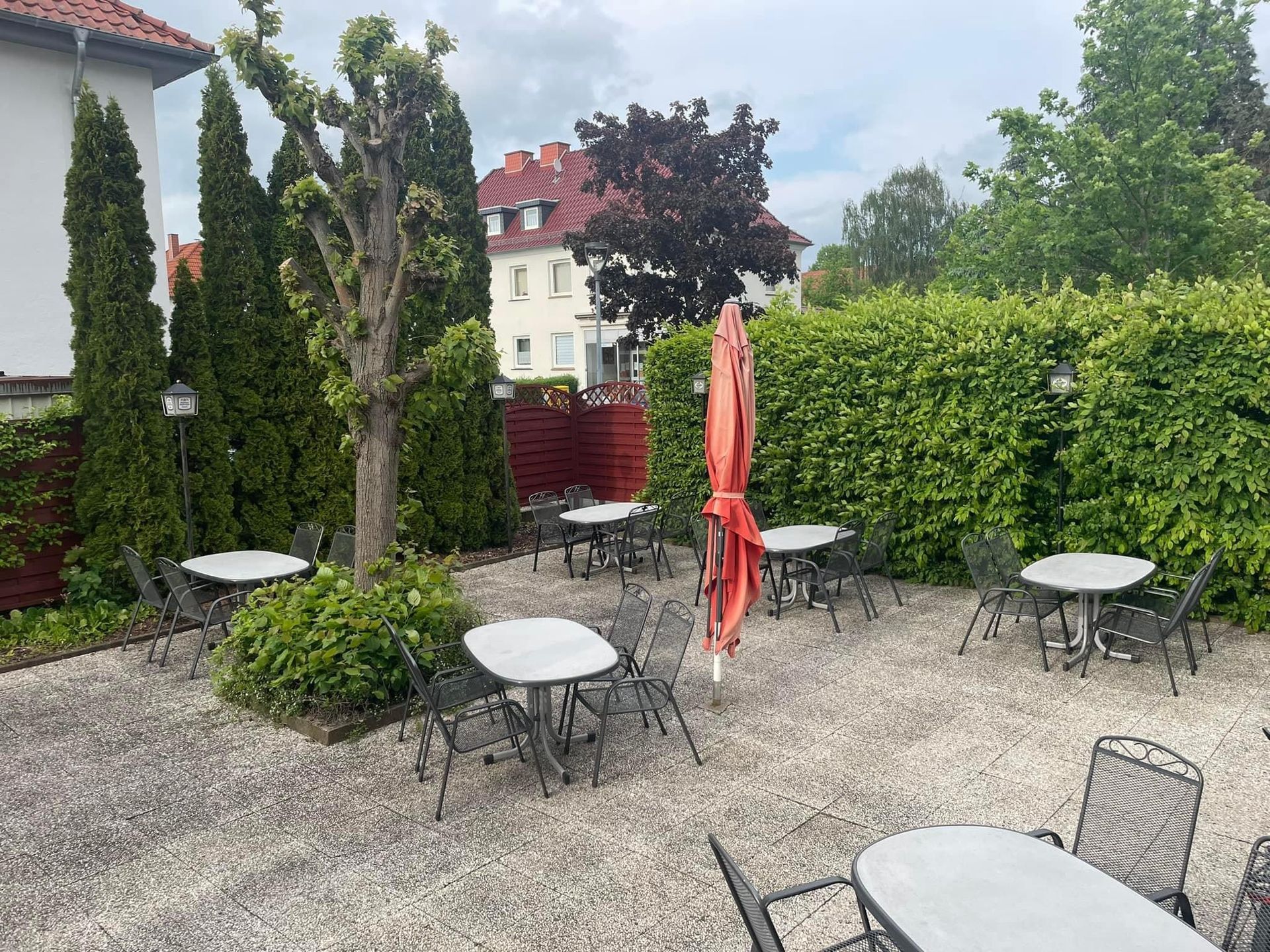 Eine Terrasse mit Tischen und Stühlen und einem roten Sonnenschirm.