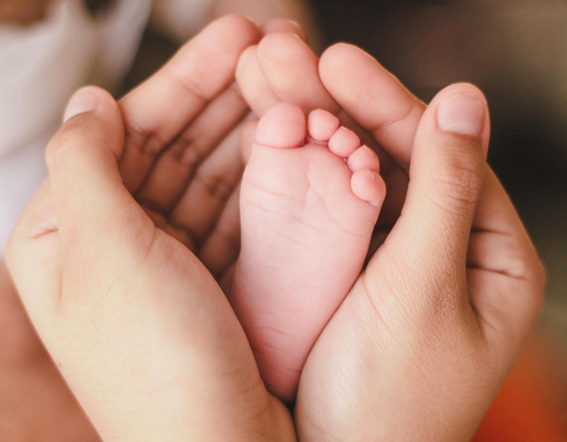Hands gently cupping a baby’s feet against a soft blurred background