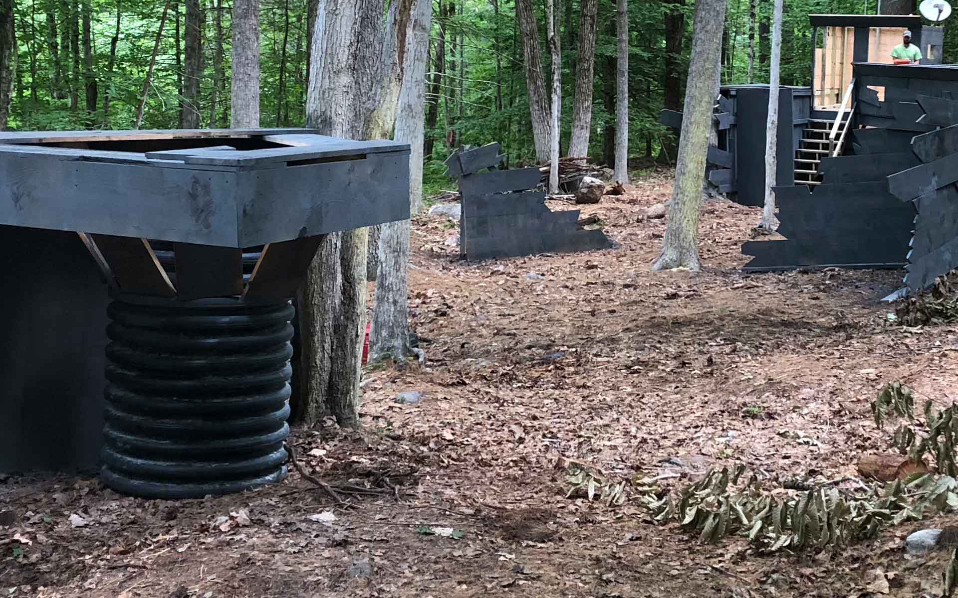 Outdoor laser tag arena with dark gray bunkers in a wooded area.