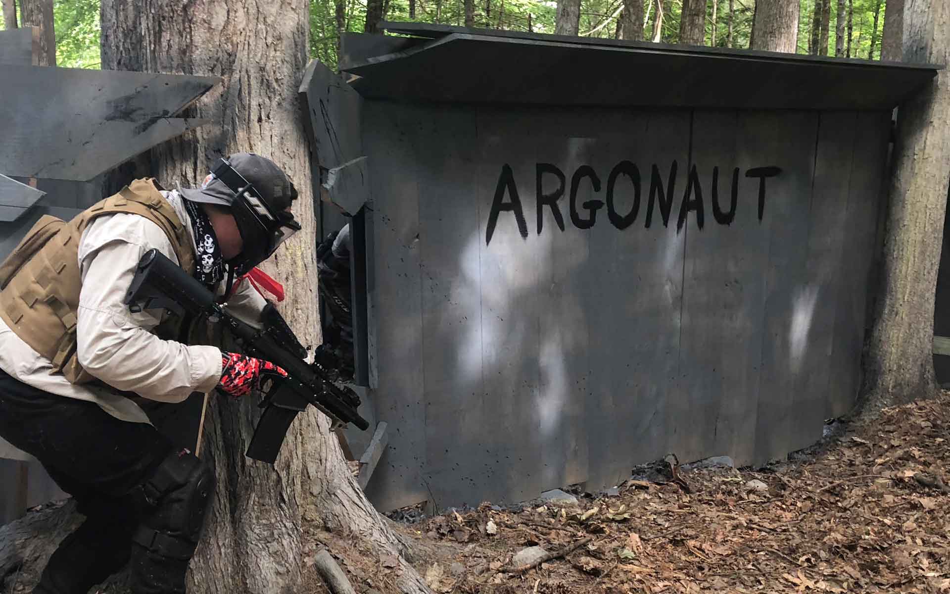 A person in tactical gear aims a rifle at a bunker marked