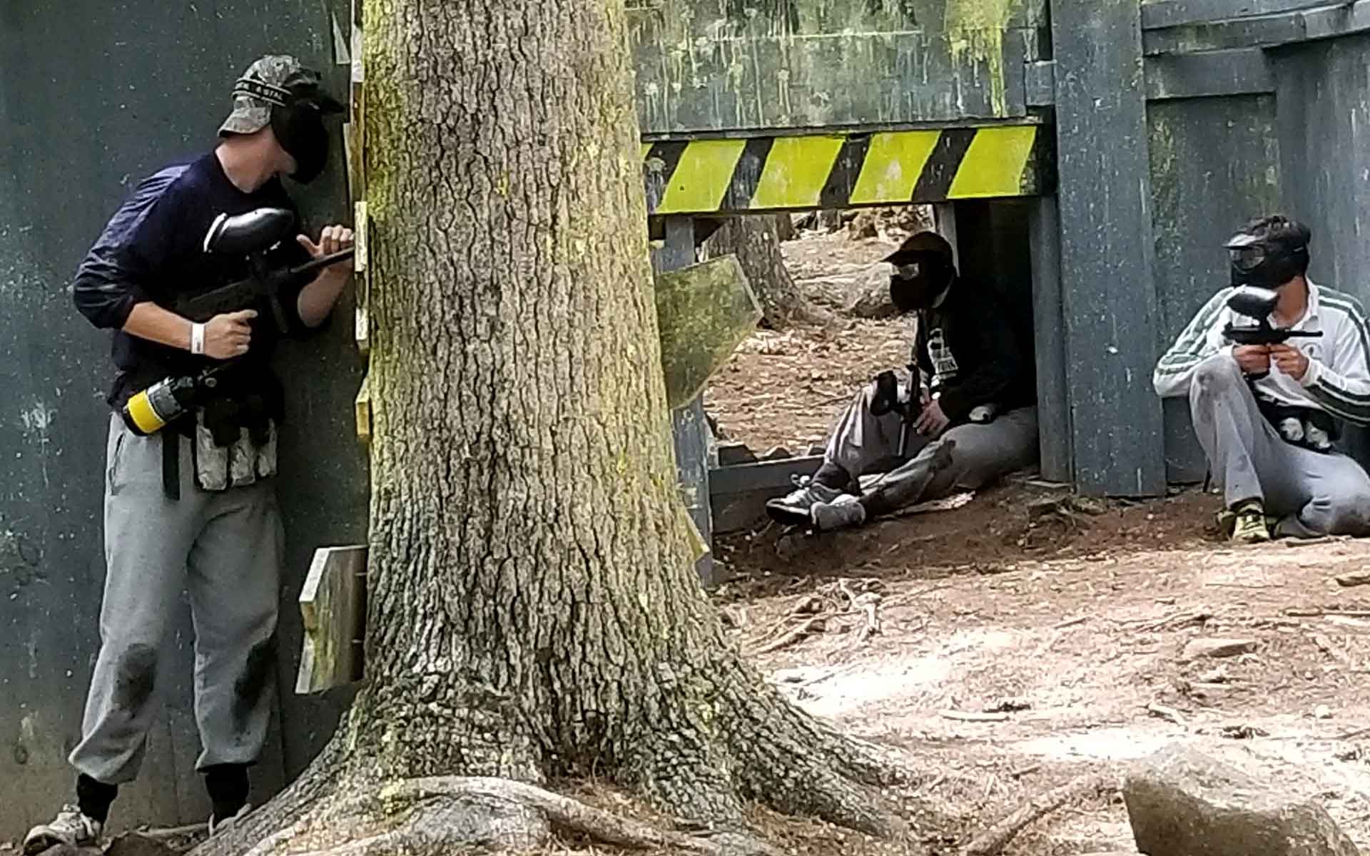 People playing paintball in a wooded area, aiming paintball guns.