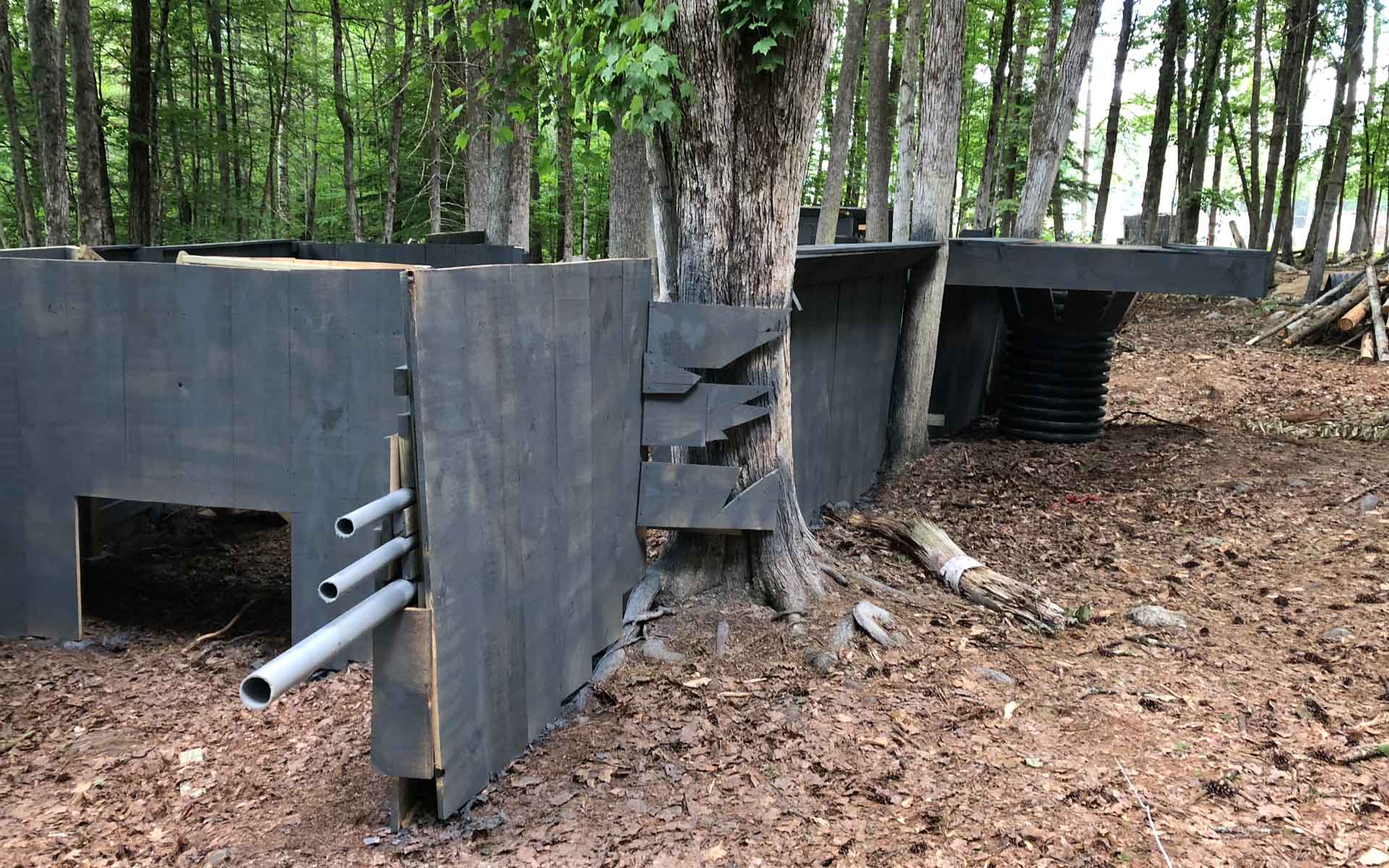 Black wooden barriers in a forest, used as bunkers. Three pipes protrude from one side.
