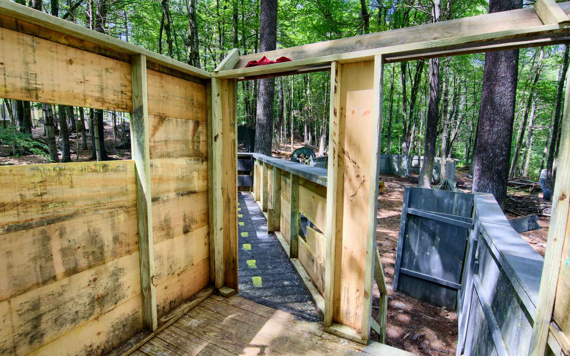 Wooden paintball structures in a wooded area, with a walkway and tall trees.