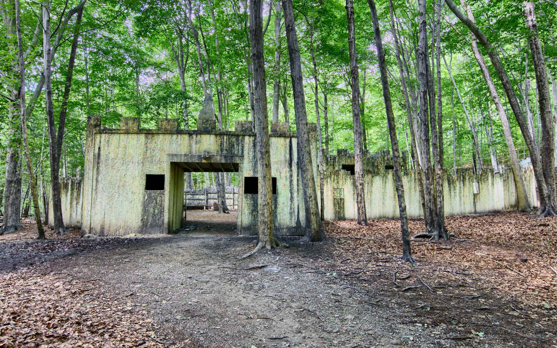 A weathered, beige paintball fort with open doorway in a forest, splattered with paint.
