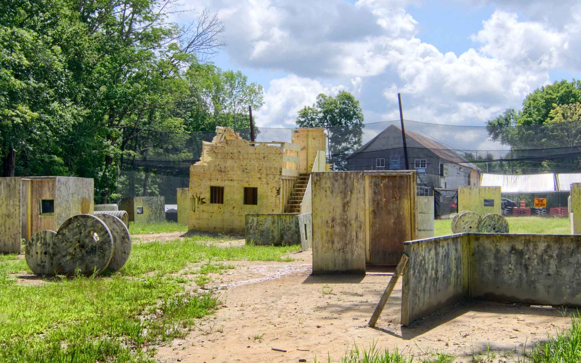 Paintball field with yellow structures, trees, and a cloudy sky.