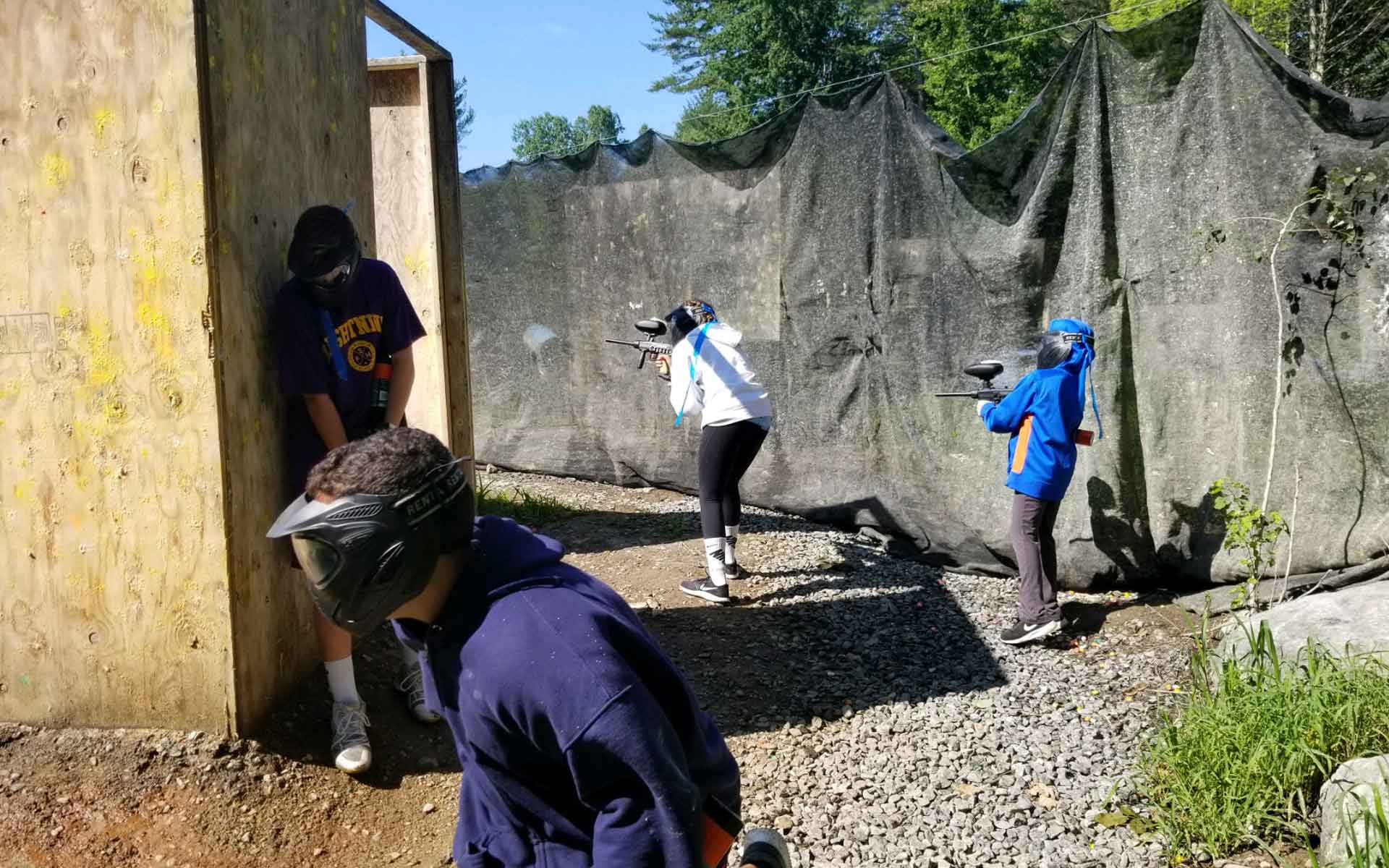 People playing paintball behind wooden structures and nets, aiming guns at each other.