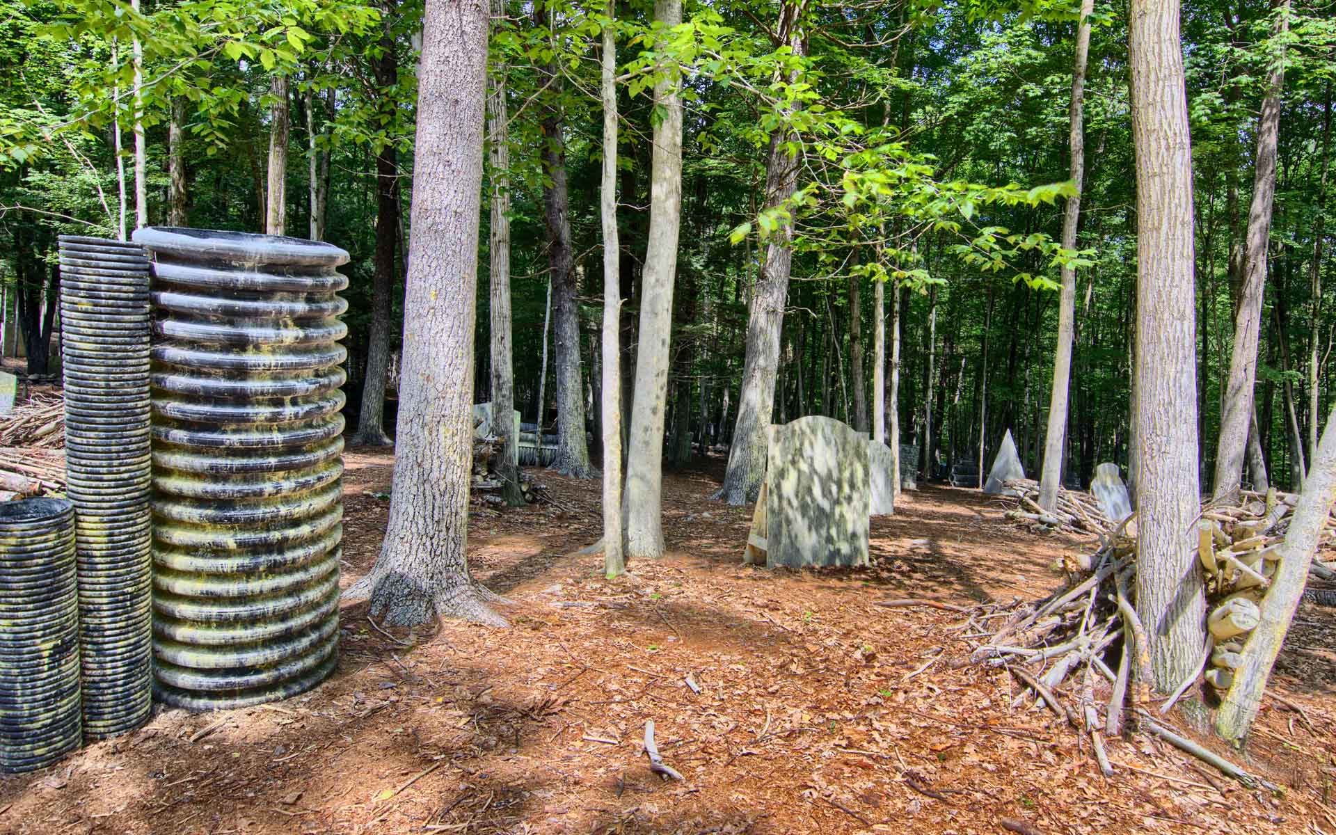 Paintball course with cylindrical bunkers, trees, and foliage in a wooded area.