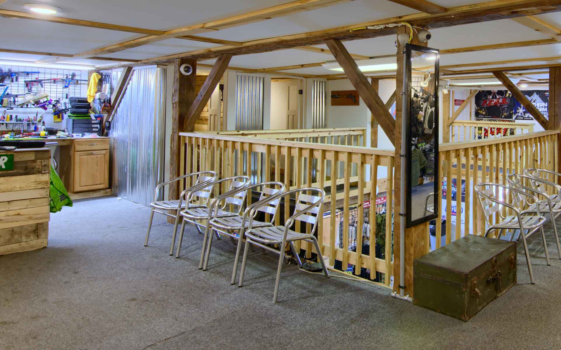 Indoor loft space with wood beams, railing, chairs, and a metal trunk.