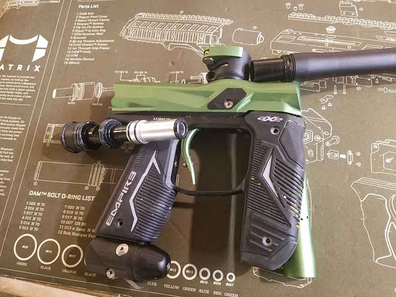 Green and black paintball gun on a green patterned mat.