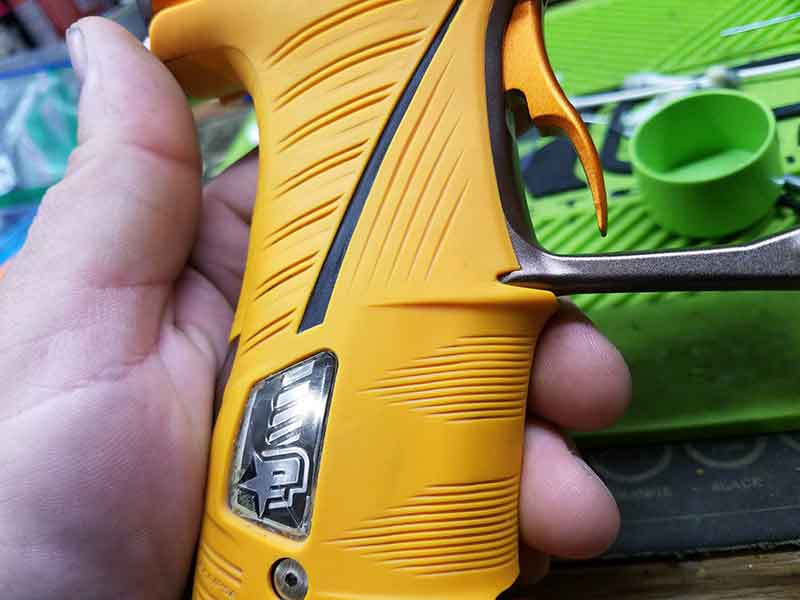 Hand holding a yellow paintball gun grip with black and silver accents.