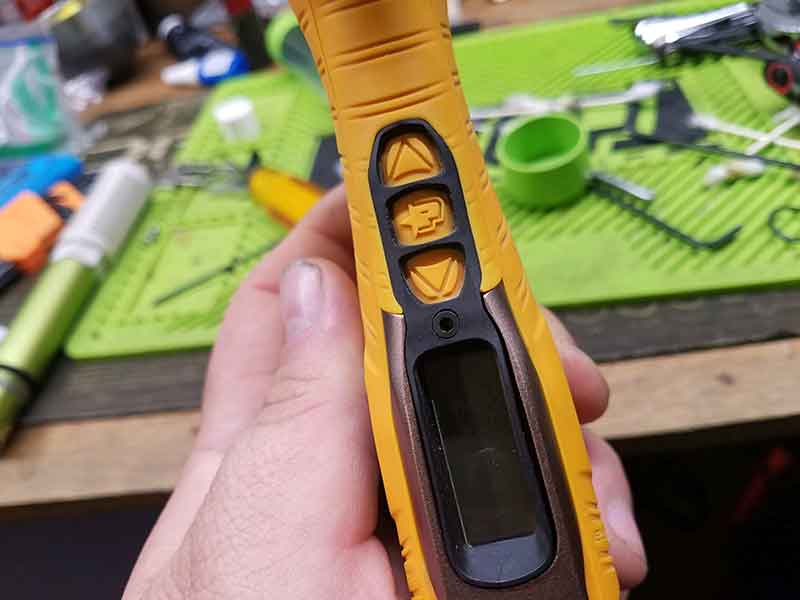 Close-up of a yellow and brown handheld device with buttons and a small screen, held in a hand.