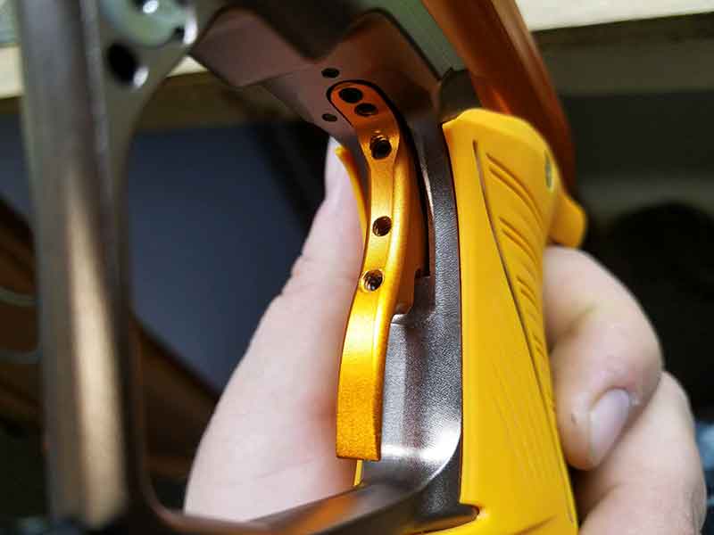 Hand holding a bright orange paintball gun trigger and grip, close-up.