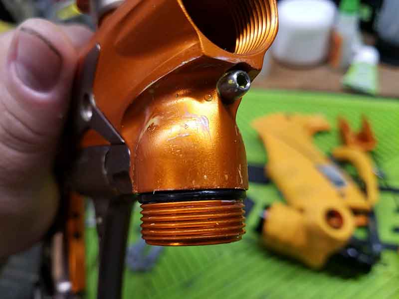 Close-up of an orange airbrush component, showing the nozzle and threaded connection with an o-ring.