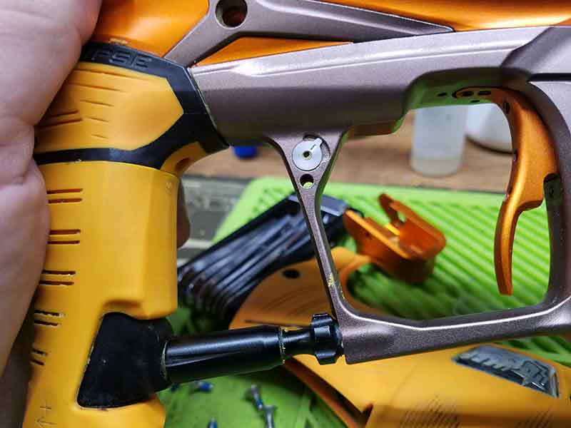Close-up of a disassembled orange and brown paintball gun frame, held in a hand.