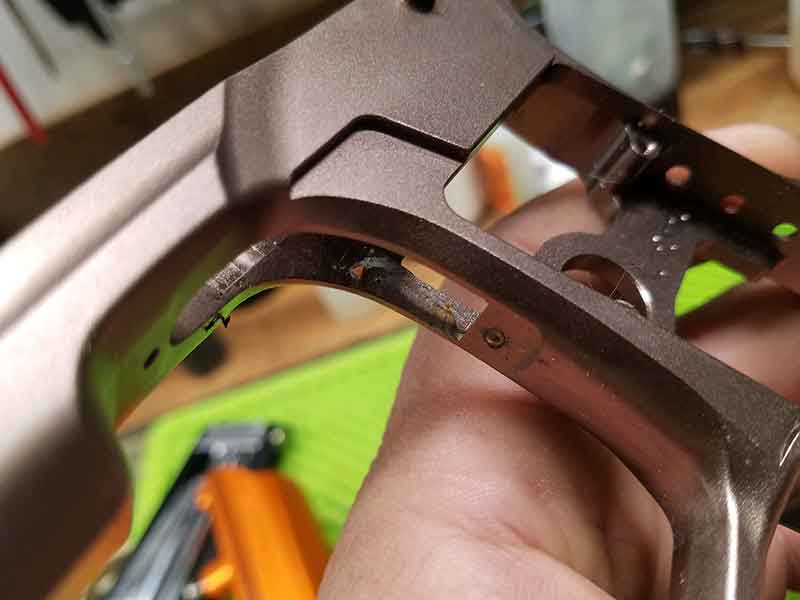 Close-up of a disassembled gun frame held in hand, showing inner workings with a silver and brown color scheme.