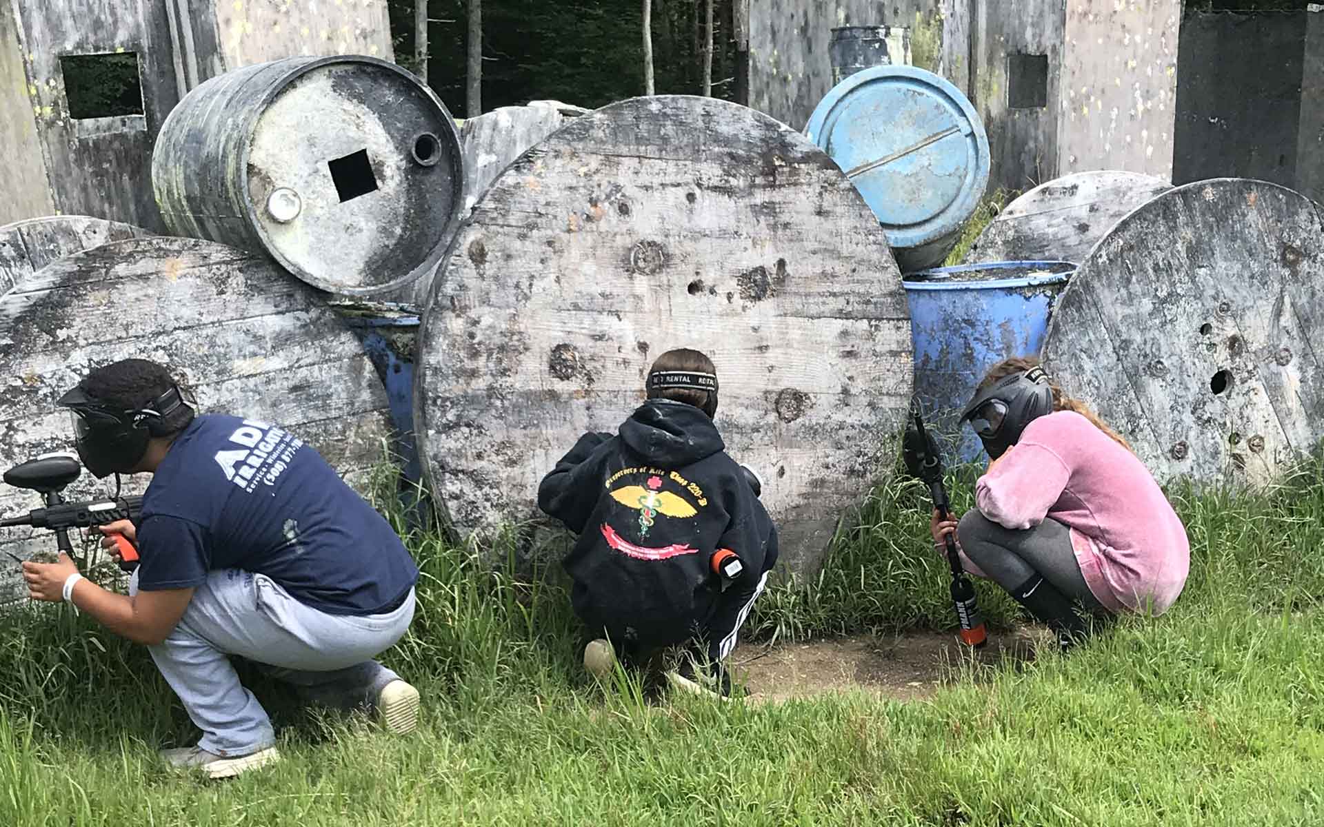 People playing paintball behind large wooden obstacles, outdoors.