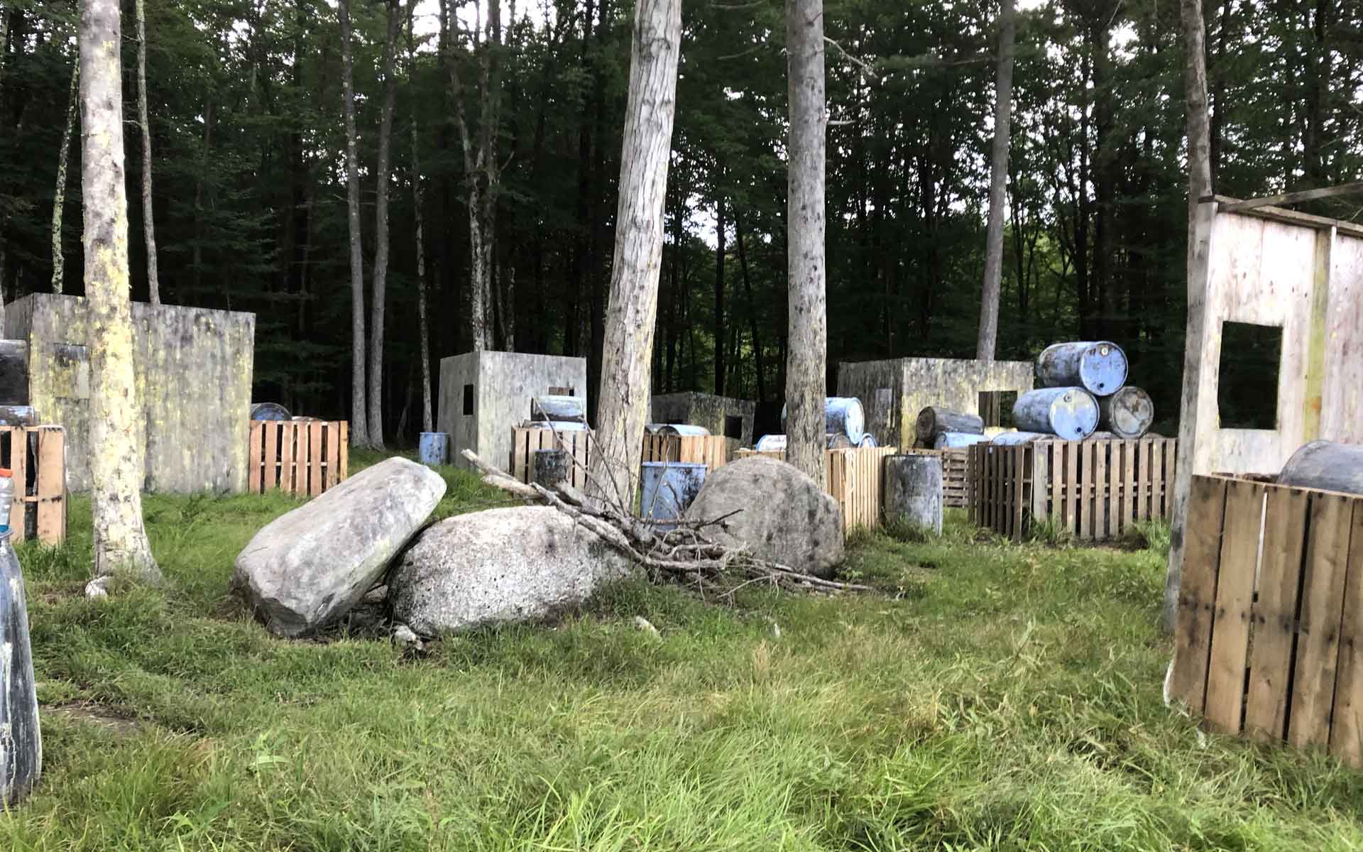 Paintball field with wooden bunkers, barrels, and trees.