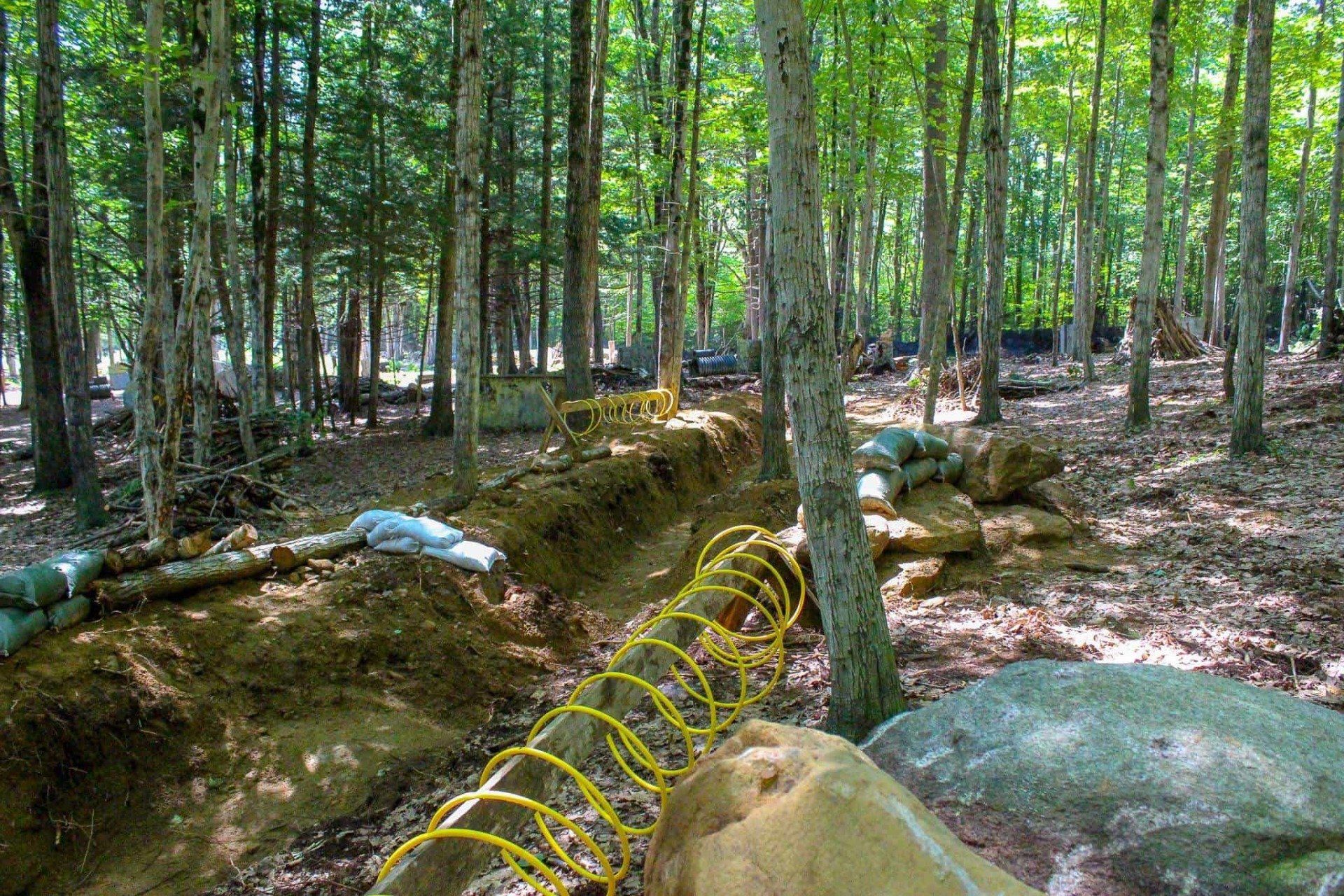 A wooded paintball field with trenches, sandbags, and yellow tubing.
