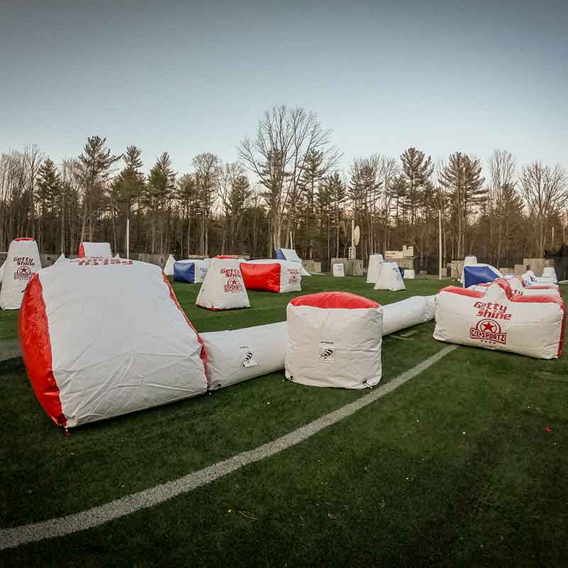 Paintball field with inflatable bunkers on a green field, trees in the background.