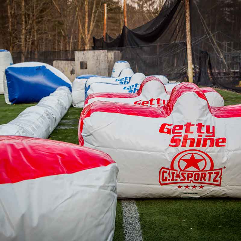 Paintball field with inflatable bunkers; red, white, and blue colors, synthetic turf, and black netting.