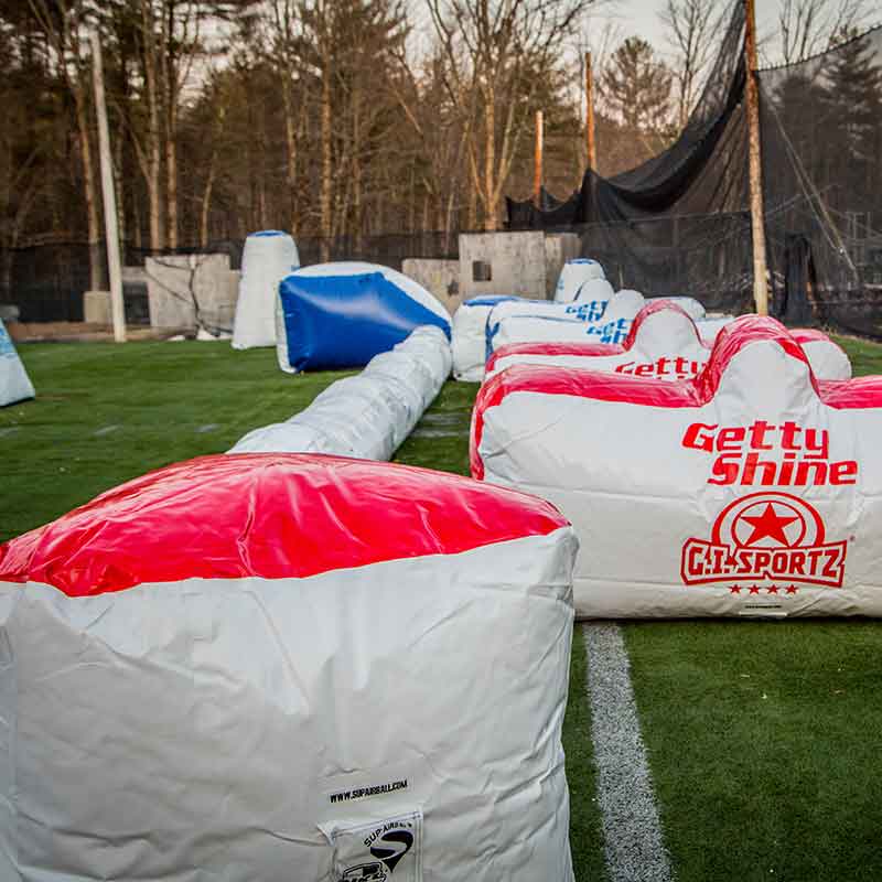 Paintball field with inflatable bunkers. Red, white, and blue obstacles on green turf.
