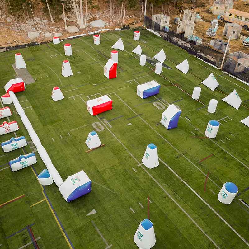 Aerial view of a paintball field with various inflatable bunkers on a green grass playing surface.