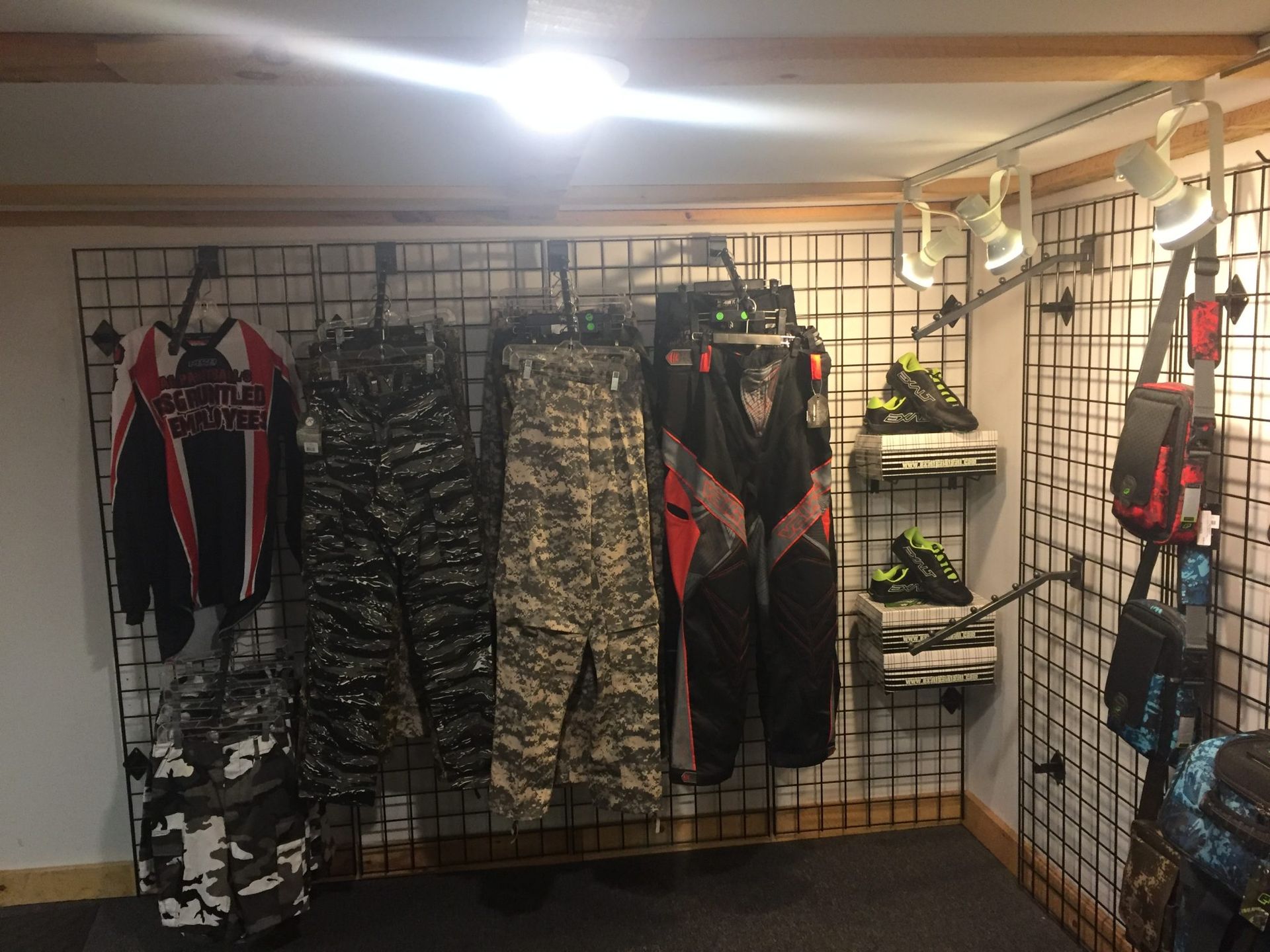 Clothing store interior, garments hanging on metal grids, including pants and jackets, black and camouflage colors.