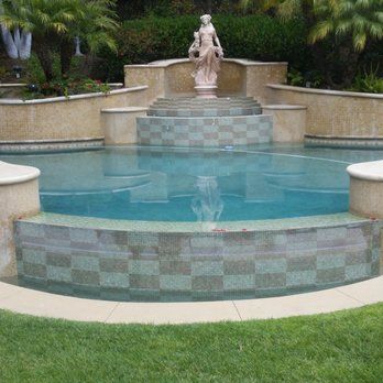 Pool with statue, tiered design, and green tile accents, surrounded by lawn.