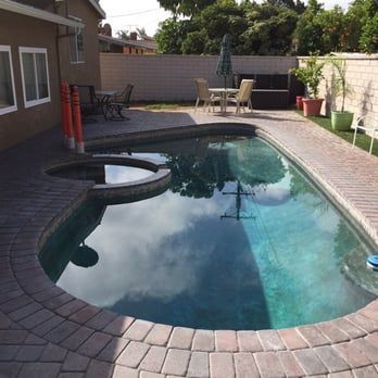 Backyard pool with brick border, hot tub, patio furniture, and green grass.