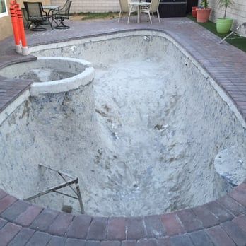 Empty swimming pool undergoing renovation, showing exposed concrete and brick surround.