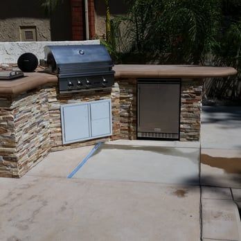 Outdoor kitchen with stone facade, grill, refrigerator, and countertop on a patio.