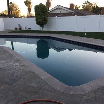 A swimming pool with a reflection of a tree and house. A white fence and green grass in the background.