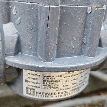 Close-up of cracked grey pool equipment with manufacturer label, with some water droplets visible.