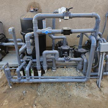Pool equipment: pipes, filters, and pumps. Gray plastic tubing against a beige wall in an outdoor setting.