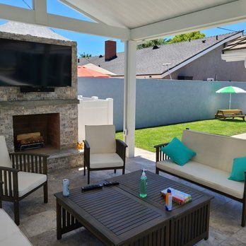 Outdoor patio with fireplace, TV, seating, and a backyard with a lawn and fence.