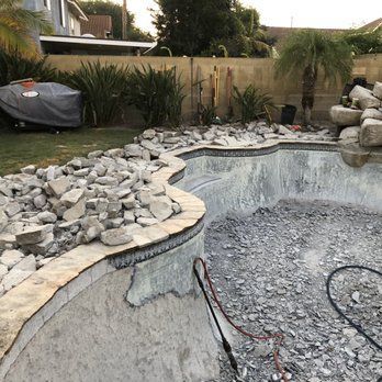 Pool being renovated with exposed concrete and rubble. Rocks and debris around the edges.
