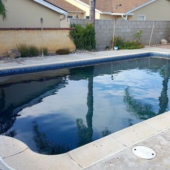 Pool with clear water, reflecting palm trees and blue sky, in a backyard setting.