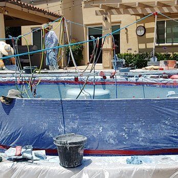 Pool renovation with blue tarp, workers, and equipment in a backyard setting.